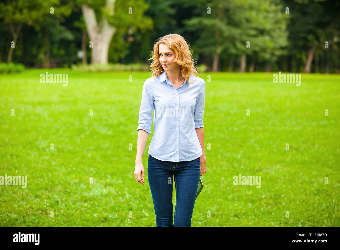 Belle jeune femme avec le comprimé dans la main, en marchant dans le parc Banque D'Images