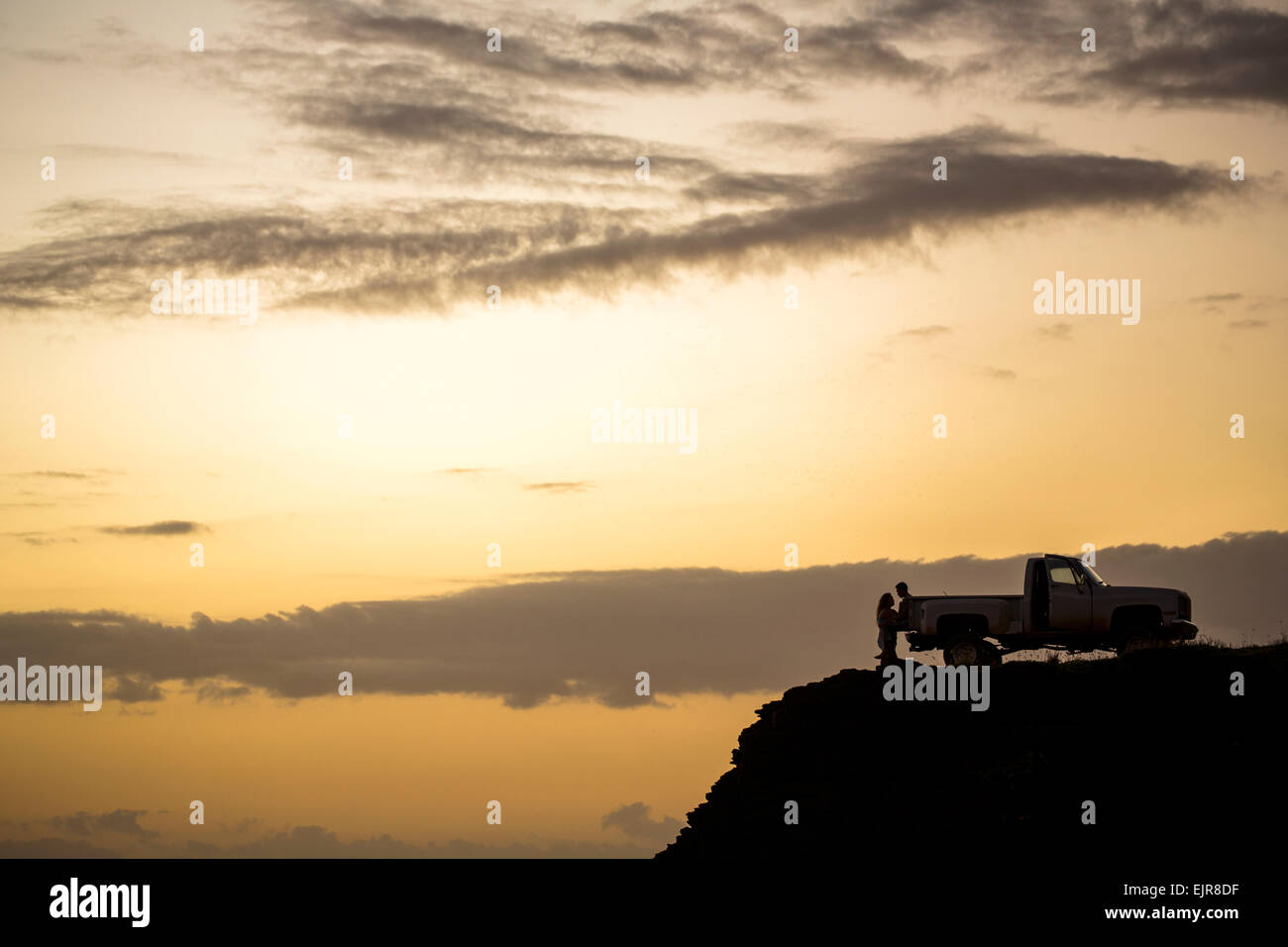 Silhouette de gens assis sur camionnette sur la falaise au coucher du soleil Banque D'Images