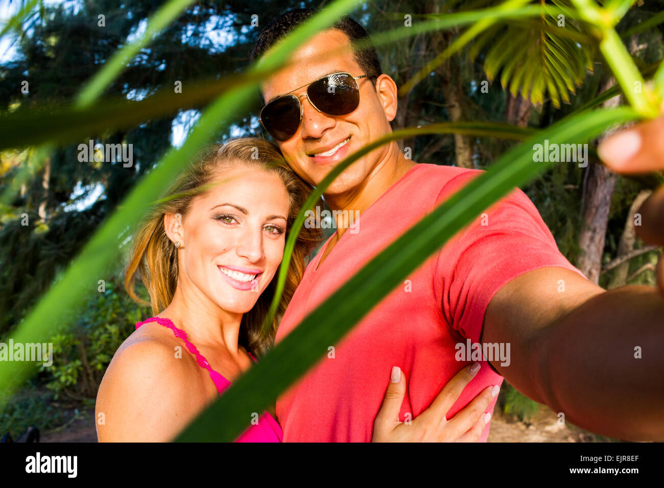 Smiling couple hugging derrière les feuilles de palmier Banque D'Images