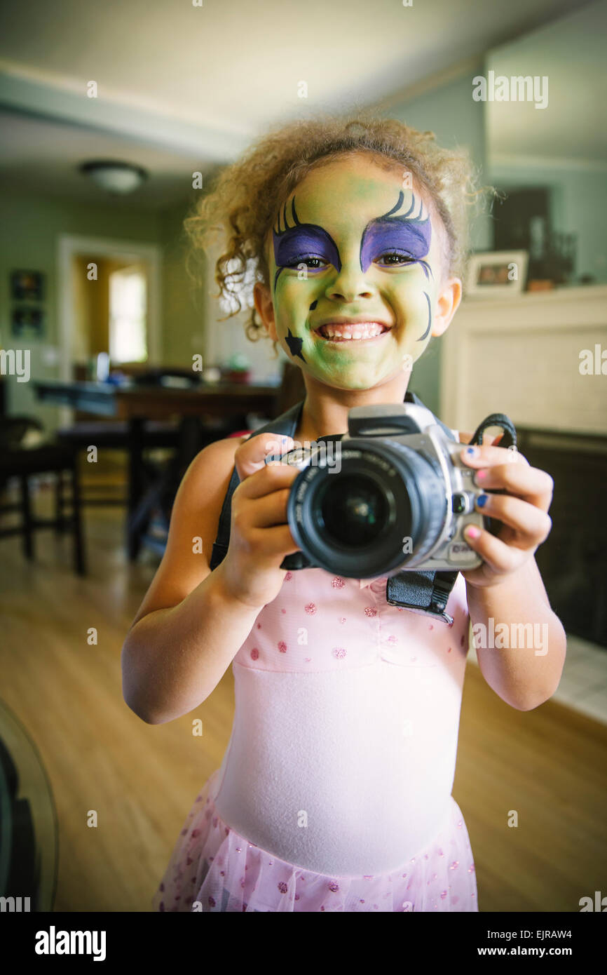 Mixed Race girl à la peinture pour le visage de photographier avec l'appareil photo Banque D'Images