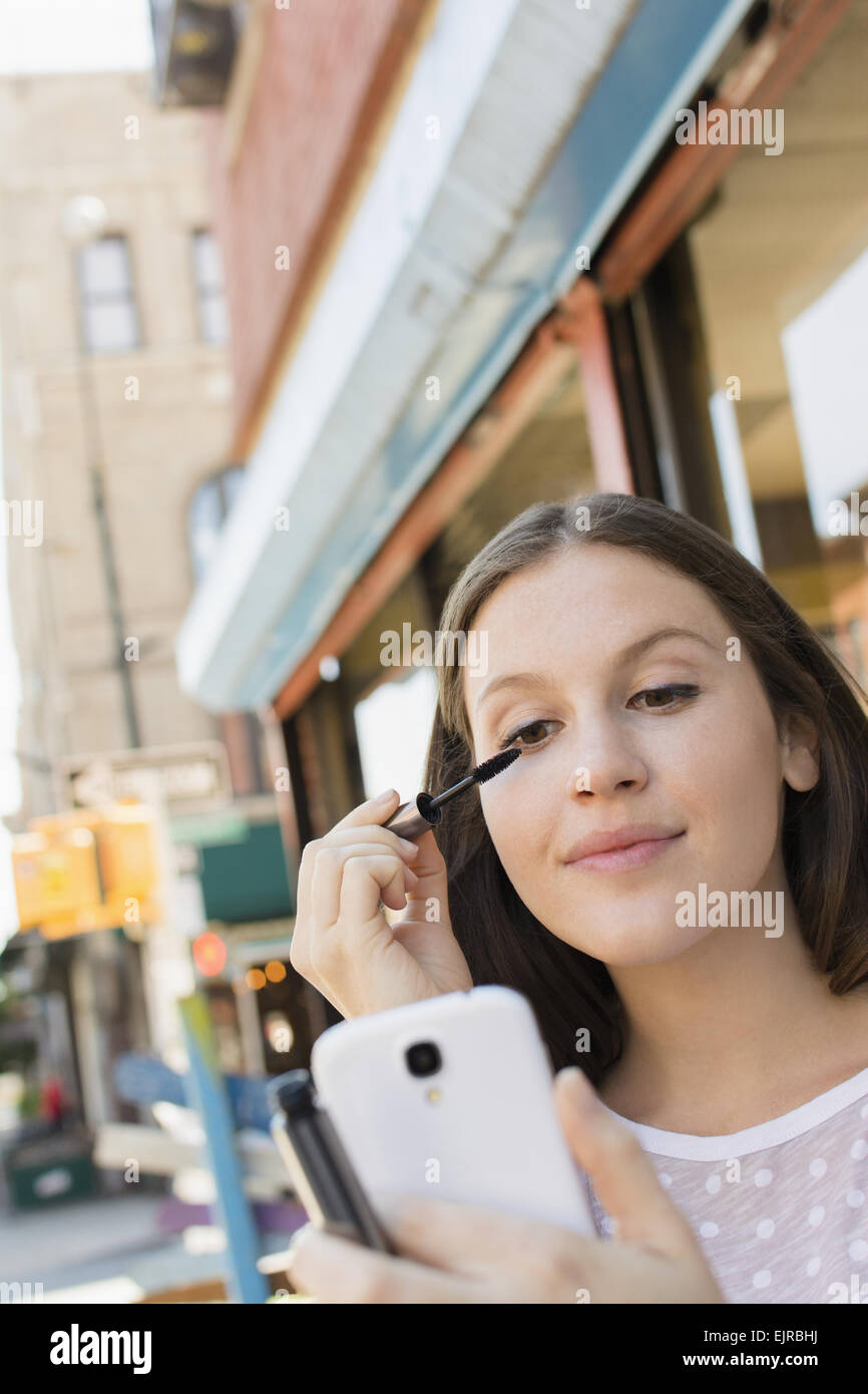 Caucasian woman applying makeup dans un téléphone cellulaire Banque D'Images