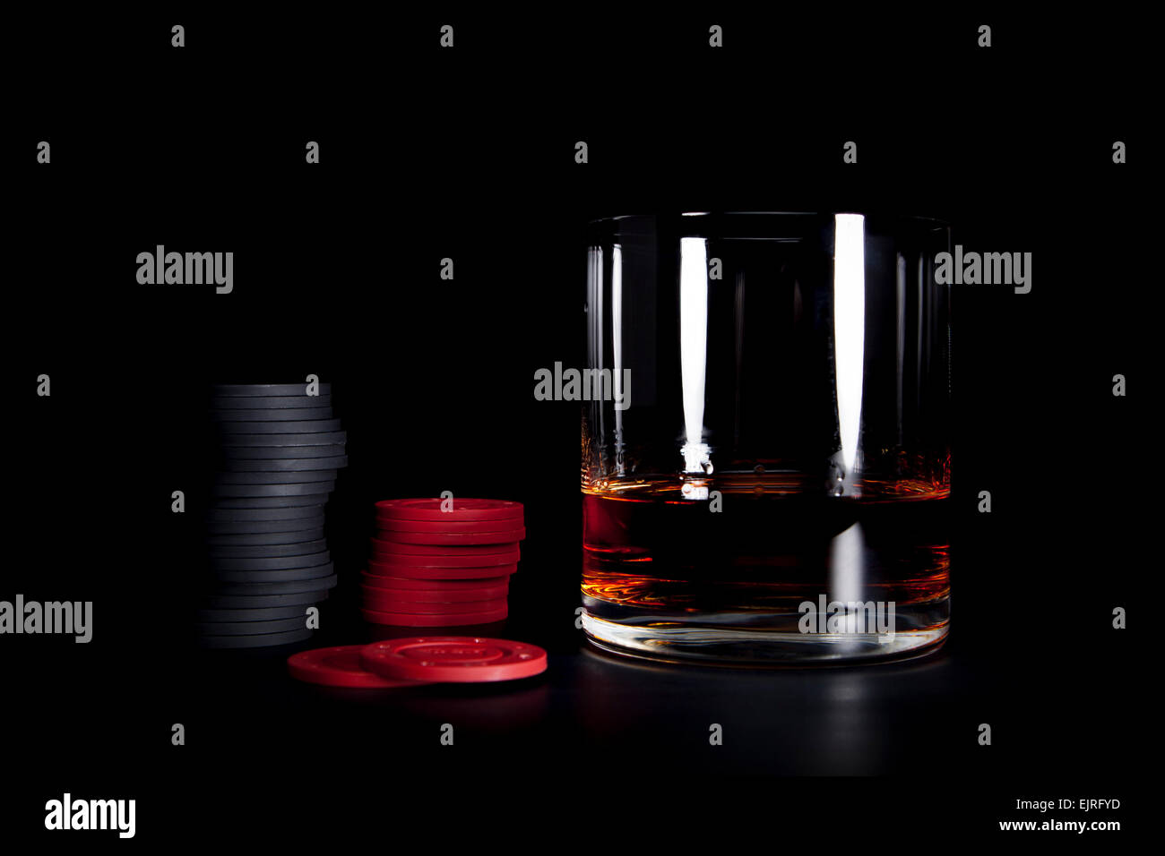 Un petit verre de cognac se trouve à côté de jetons de poker rouge et noir sur un fond noir ; atmosphère ; moody format horizontal Banque D'Images