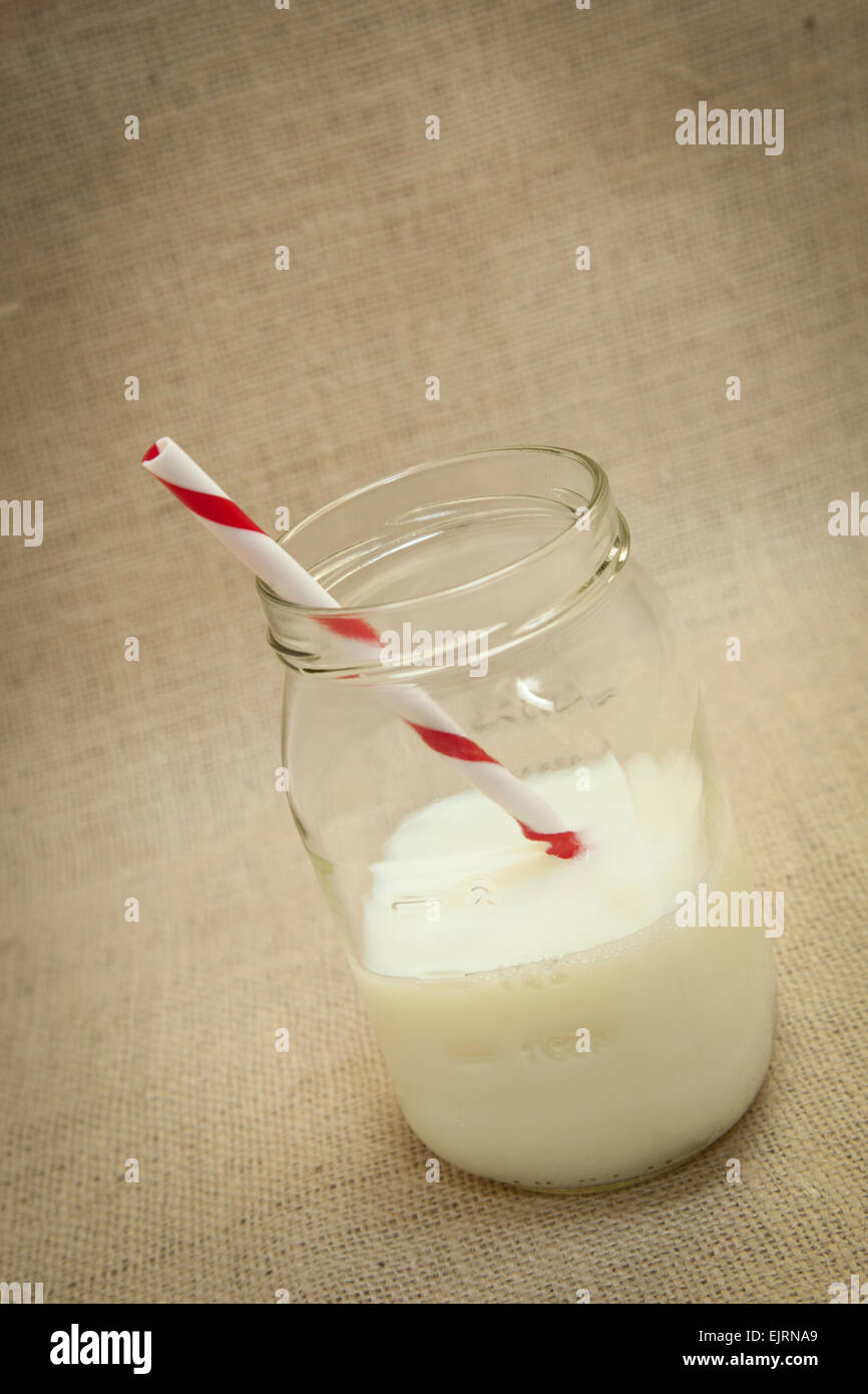 Un pot Mason est rempli avec du lait blanc, rouge et blanc paille swirl dans le lait ; fond de toile Banque D'Images Un pot Mason est rempli avec du lait blanc, rouge et blanc paille swirl dans le lait ; fond de toile Banque D'Images