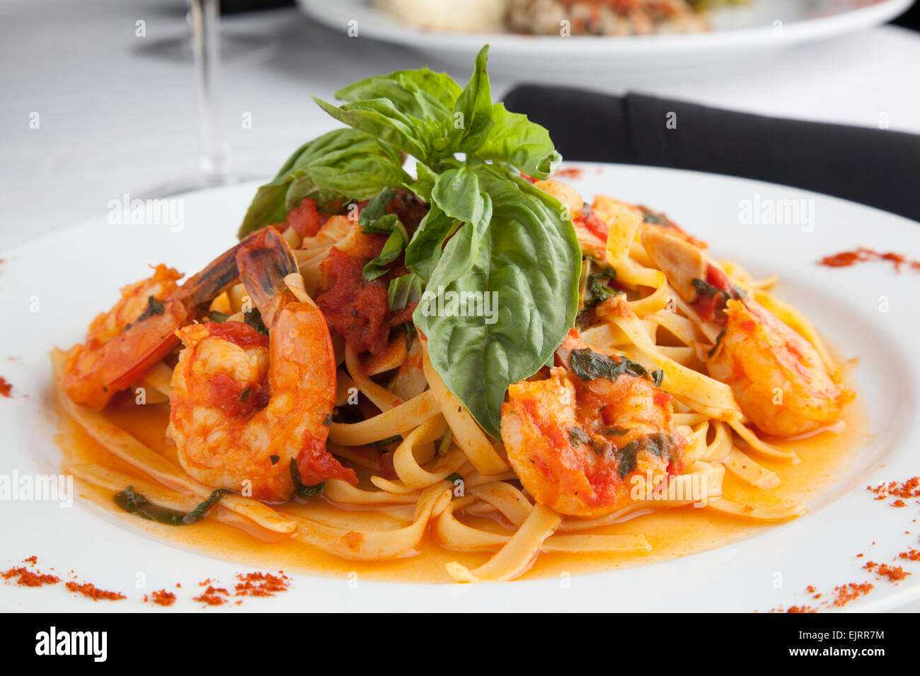 Une plaque blanche détient Linguine aux crevettes dans une sauce Fra Diavolo, garni de basilic frais. Paprika est saupoudré sur la plaque. Banque D'Images