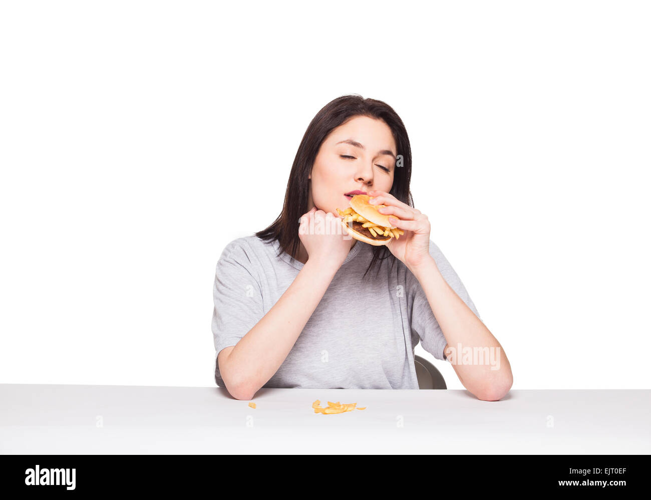 Jeune femme naturel de manger de la malbouffe, hamburger et frites, sur fond blanc Banque D'Images
