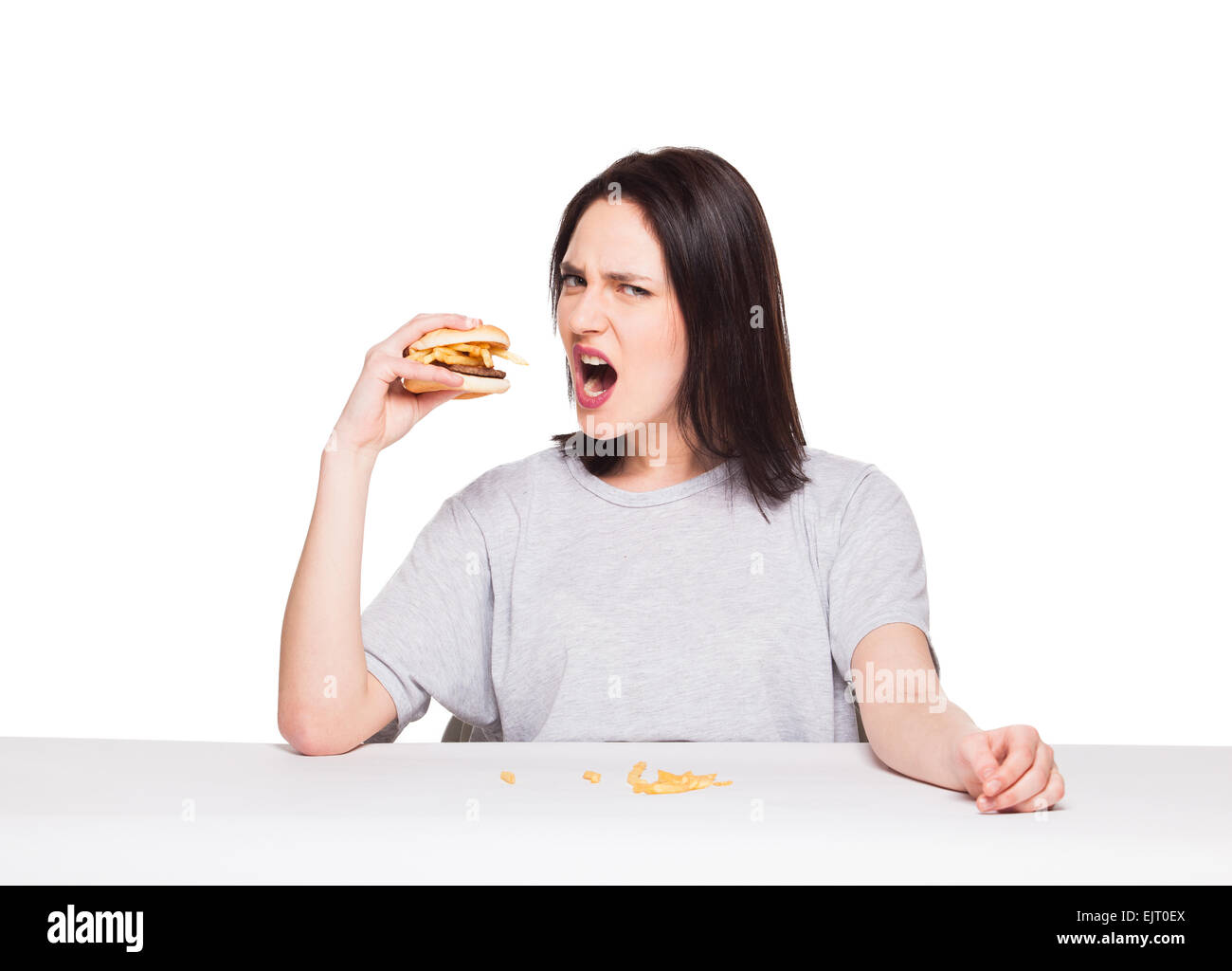 Jeune femme naturel de manger de la malbouffe, hamburger et frites, sur fond blanc Banque D'Images