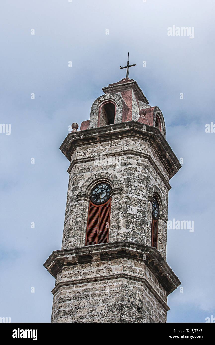 L'une des tours en pierre de la cathédrale Saint Christophe dans la vieille Havane à Cuba avec un fond nuageux et réveil et crucifix Banque D'Images