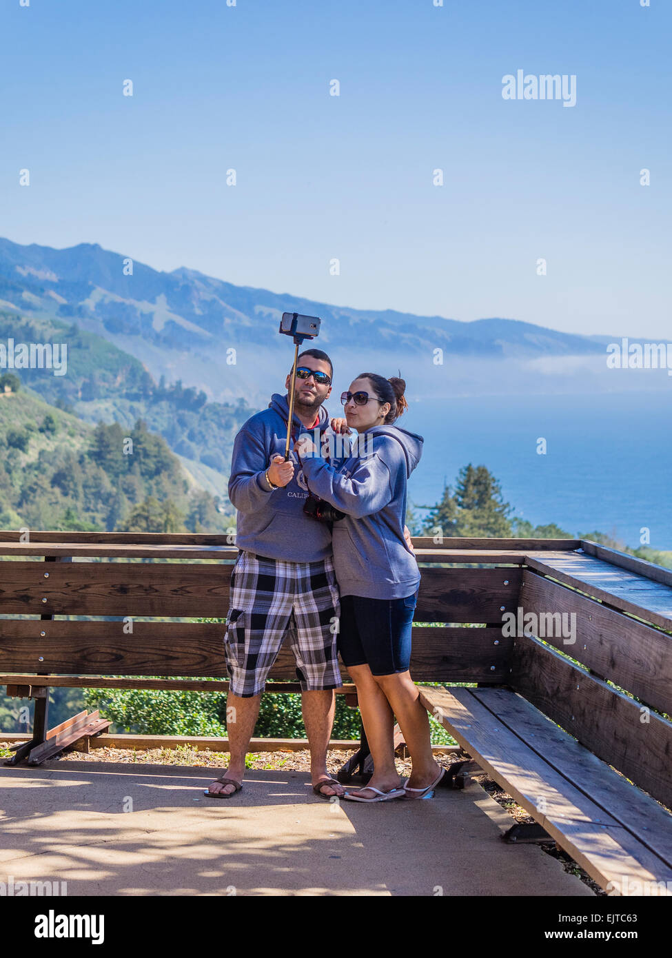 Un jeune couple en vacances prendre un autoportrait à l'aide d'un bâton selfies avec leur smartphone à Big Sur, en Californie. Banque D'Images