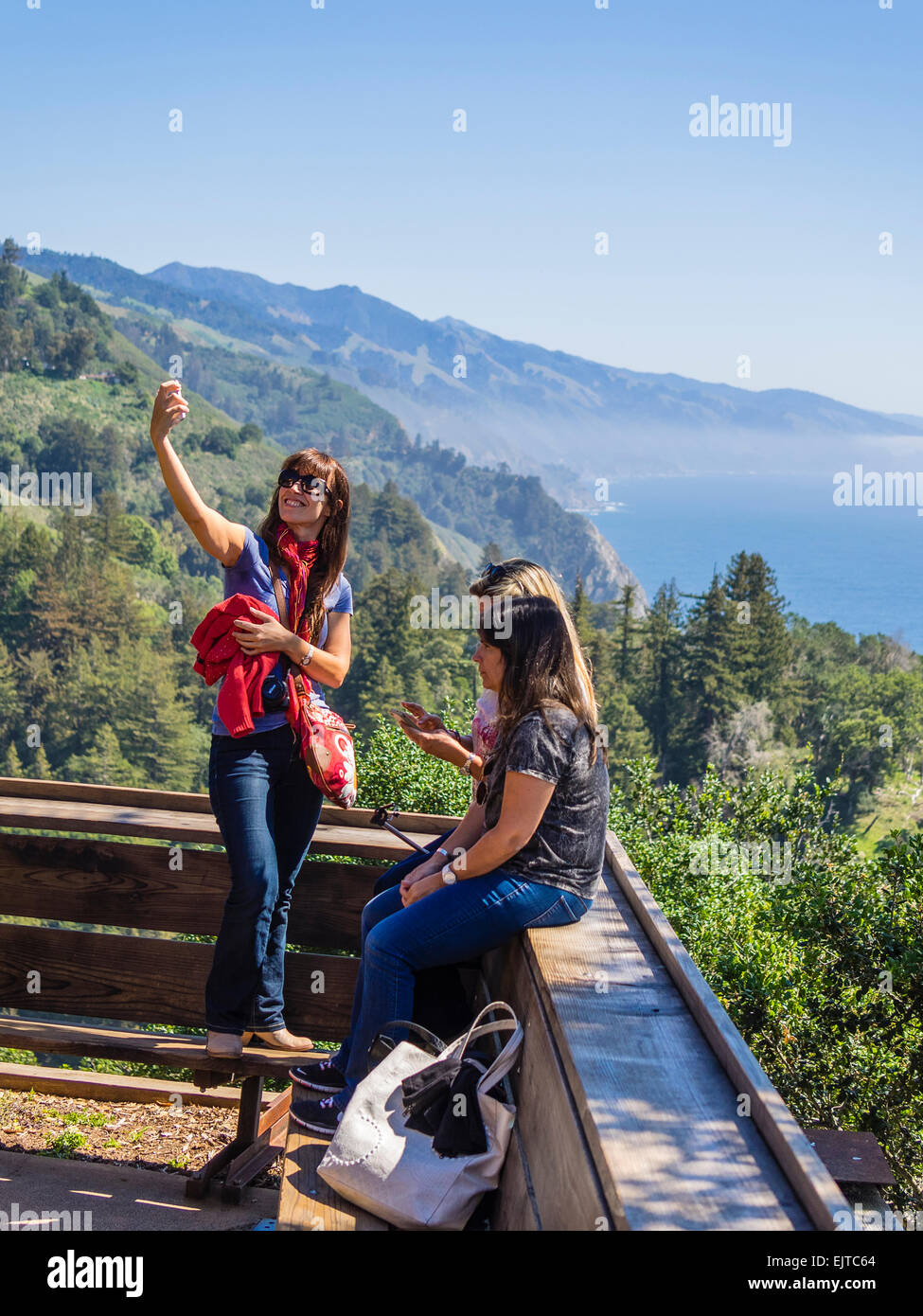 Une jeune femme prend un avec son smartphone selfies avec la côte de l'océan Pacifique et les montagnes de Big Sur, CA. Banque D'Images