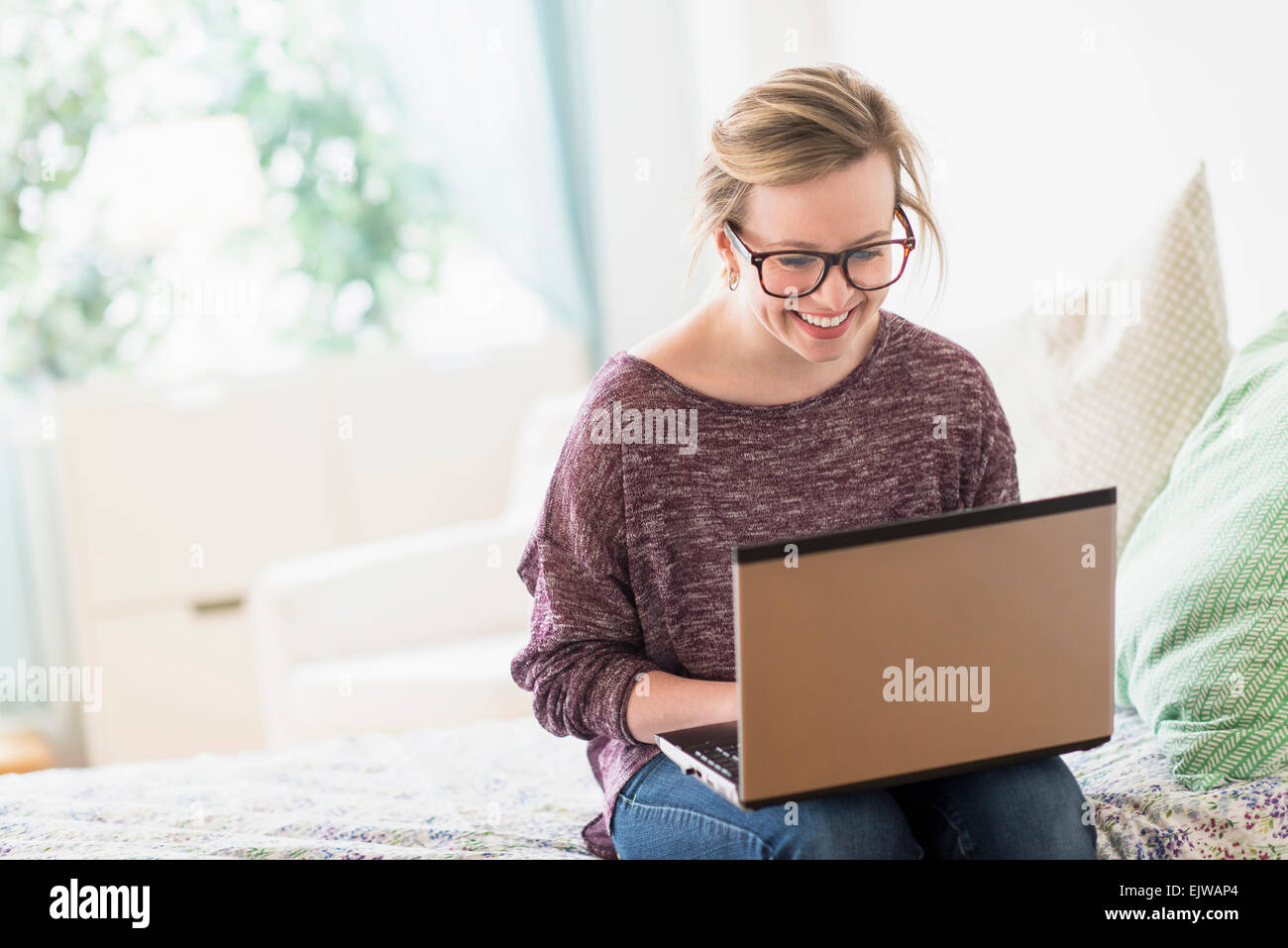 Young woman sitting on bed and using laptop Banque D'Images