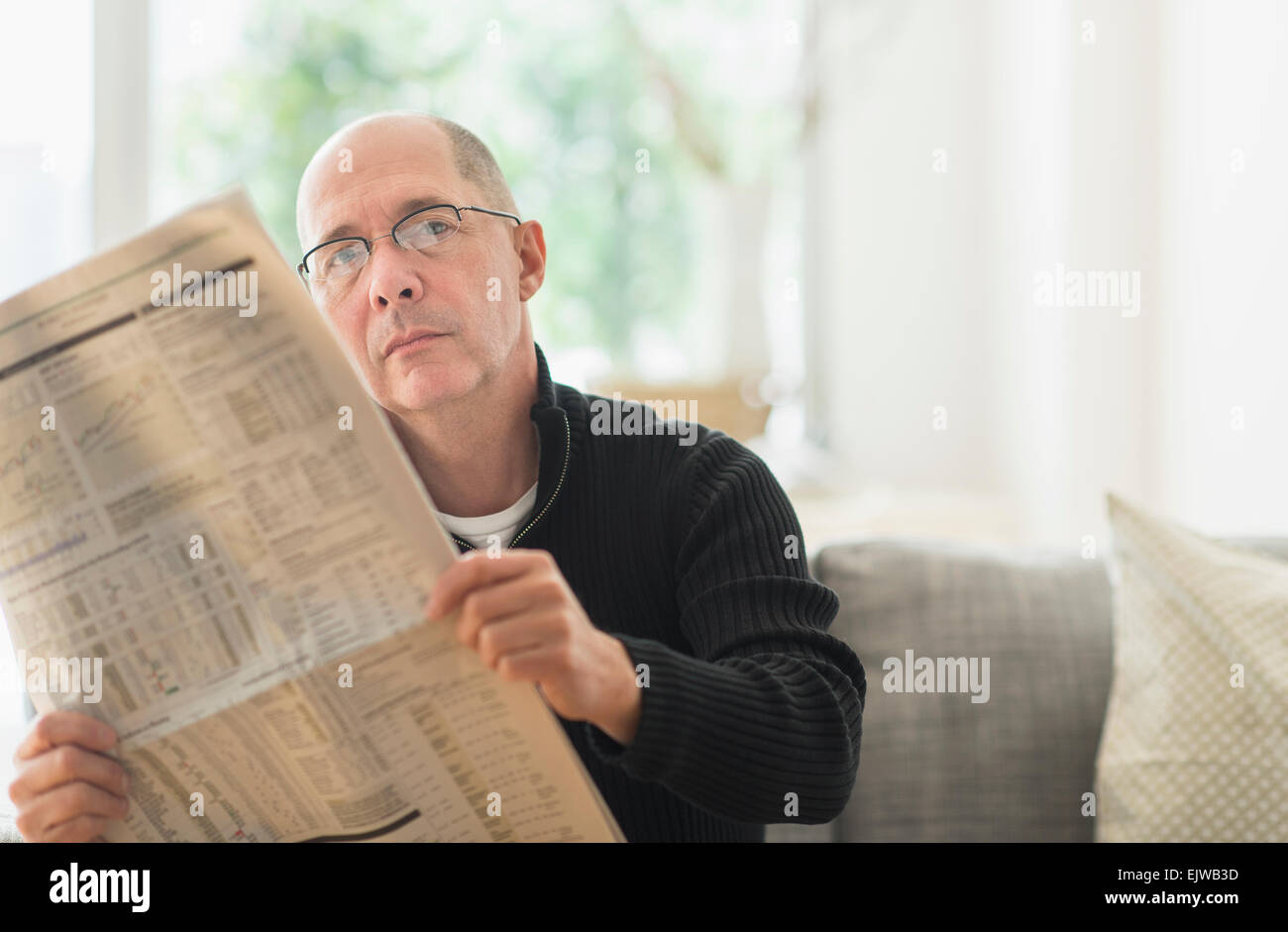 Man reading newspaper on sofa Banque D'Images