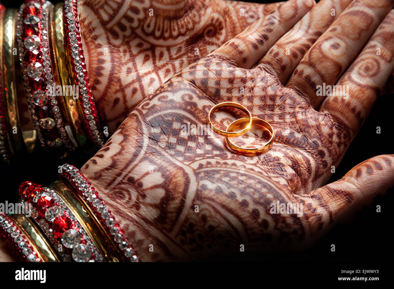 Les mains de henné femme tenant deux bagues d'or sur fond noir Banque D'Images
