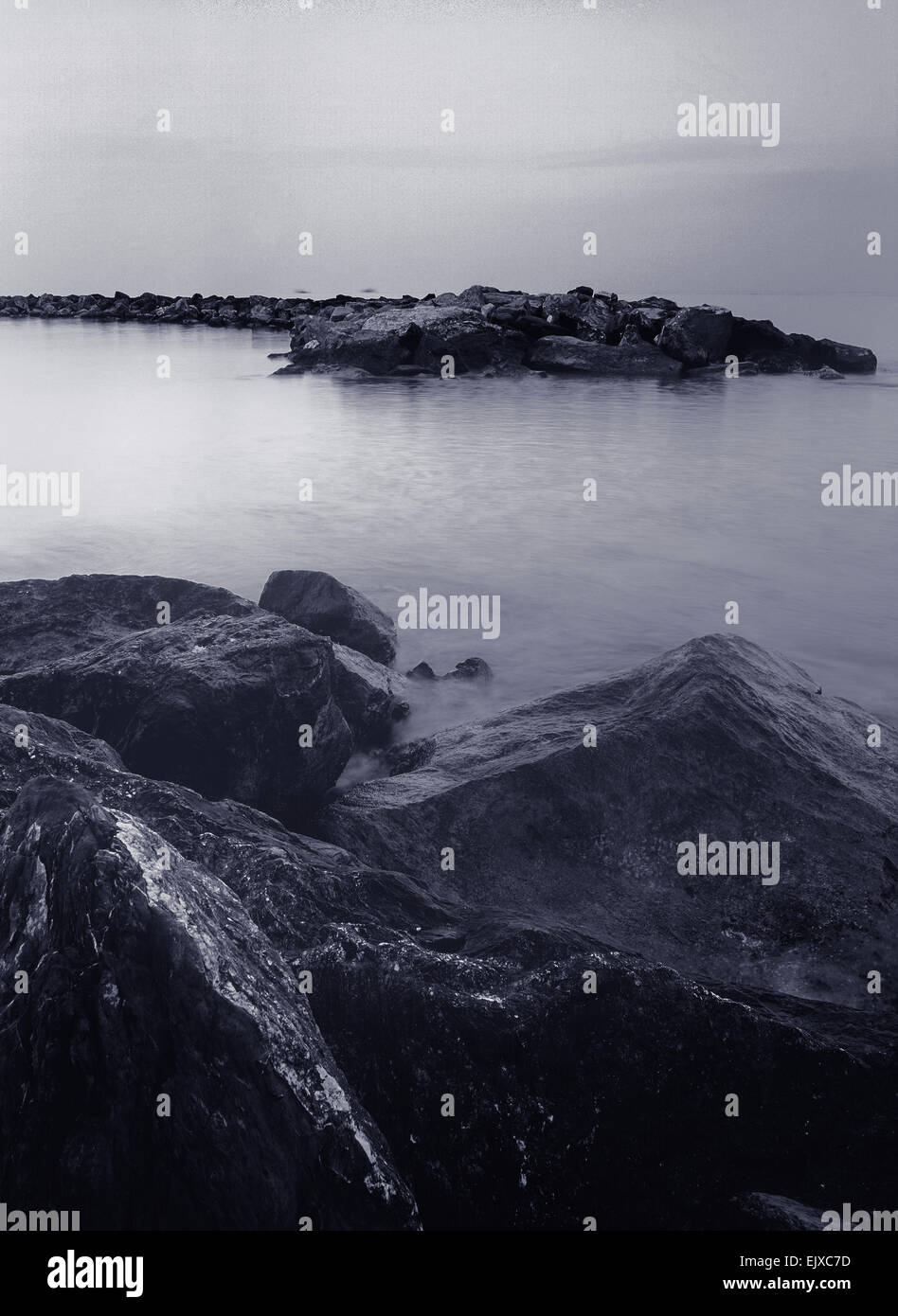 L'exposition longue verticale de format moyen avec des roches seascape monochrome à l'avant-plan et une mer calme à l'arrière-plan. Banque D'Images
