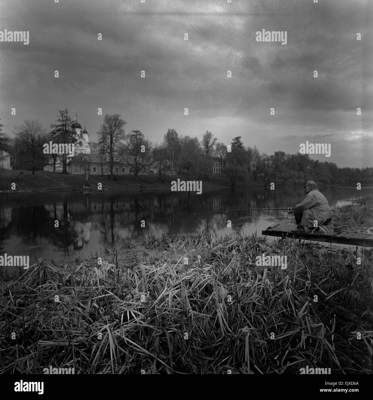 Moyen format noir et blanc numérisation de film d'un homme avec une canne à pêche à la ligne de pont en bois dans l'étang avec toujours à l'arrière de l'église Banque D'Images