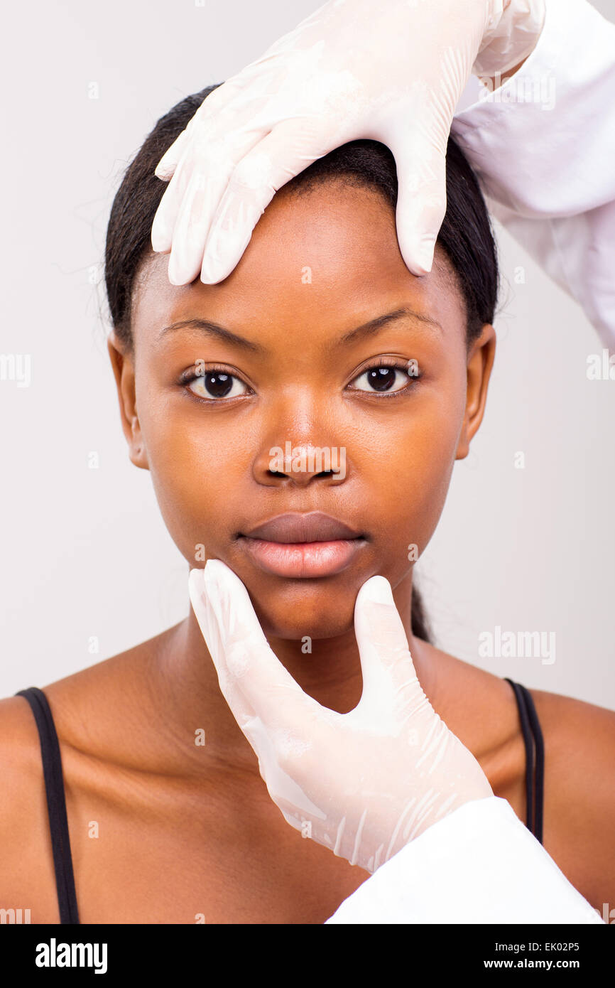 Médecin contrôle African girl face avant la chirurgie plastique sur fond uni Banque D'Images