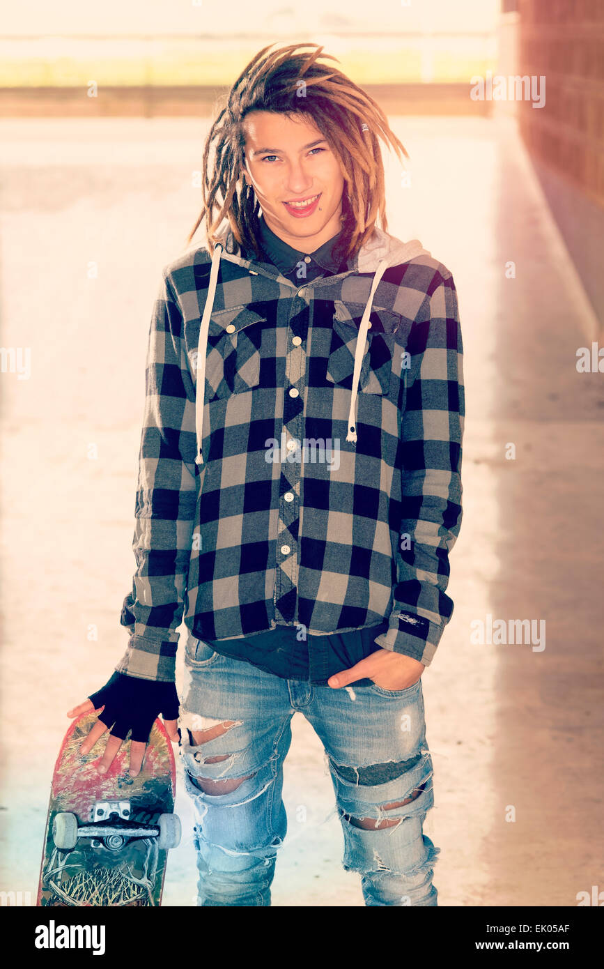 Portrait de jeune homme avec des cheveux rasta et skateboard dans un concept de vie filtre appliqué à chaud Banque D'Images