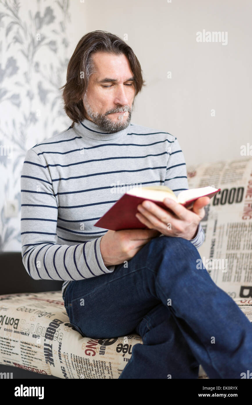 Homme barbu en lisant un livre dans le salon Banque D'Images