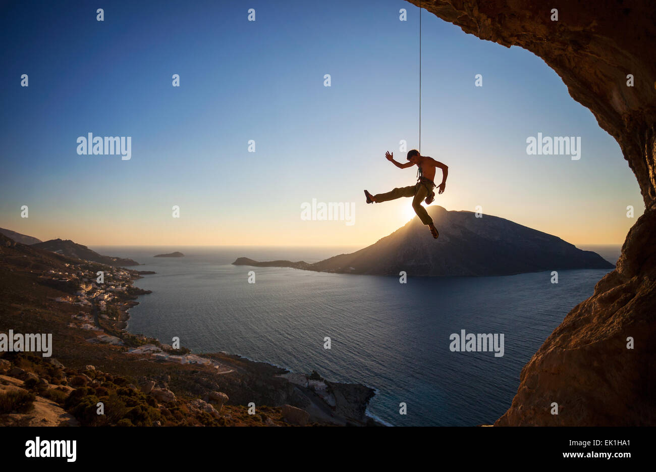 Rock climber hanging sur corde tout en escalade au coucher du soleil, avec en arrière-plan l'île de Telendos Banque D'Images