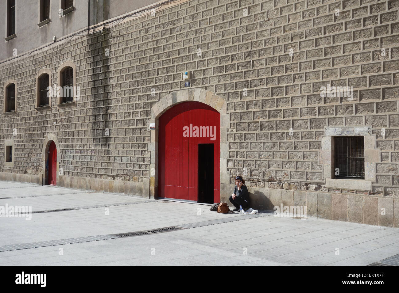 Femme assise sur le sol à l'extérieur de l'ancien bâtiment, talking on cell phone, sur une place de Barcelone, Catalogne, Espagne Banque D'Images