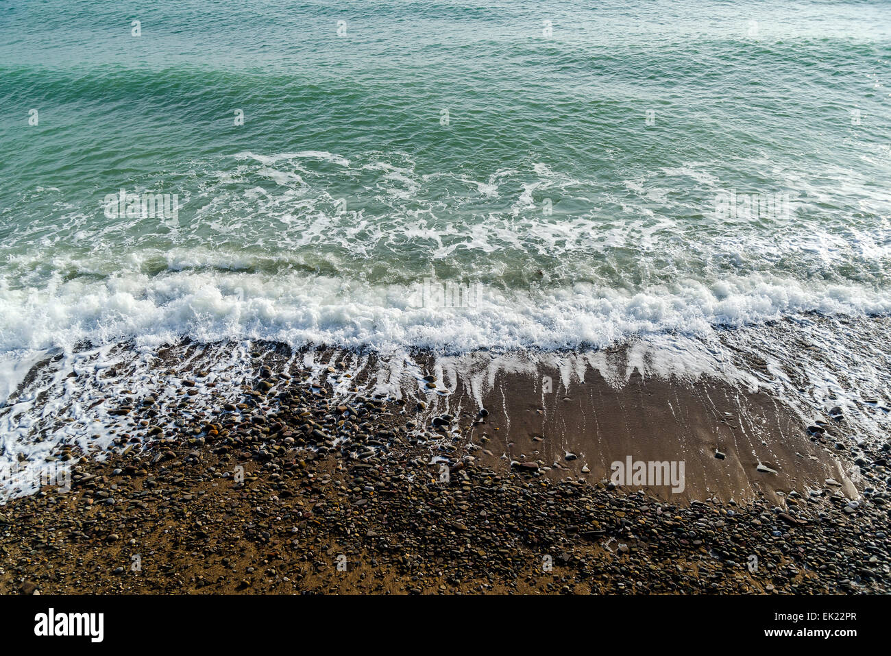 Sable mer baignée par la mer vague mousse sur la plage au lever du soleil Banque D'Images