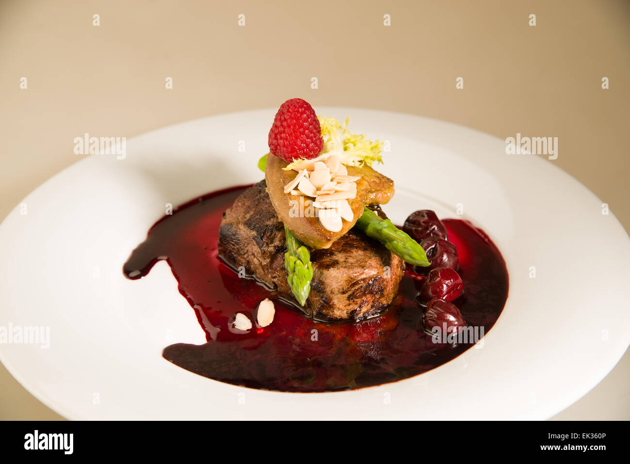 Morceau de viande rôtie à la sauce aux cerises, asperges, de framboise sur une plaque blanche Banque D'Images