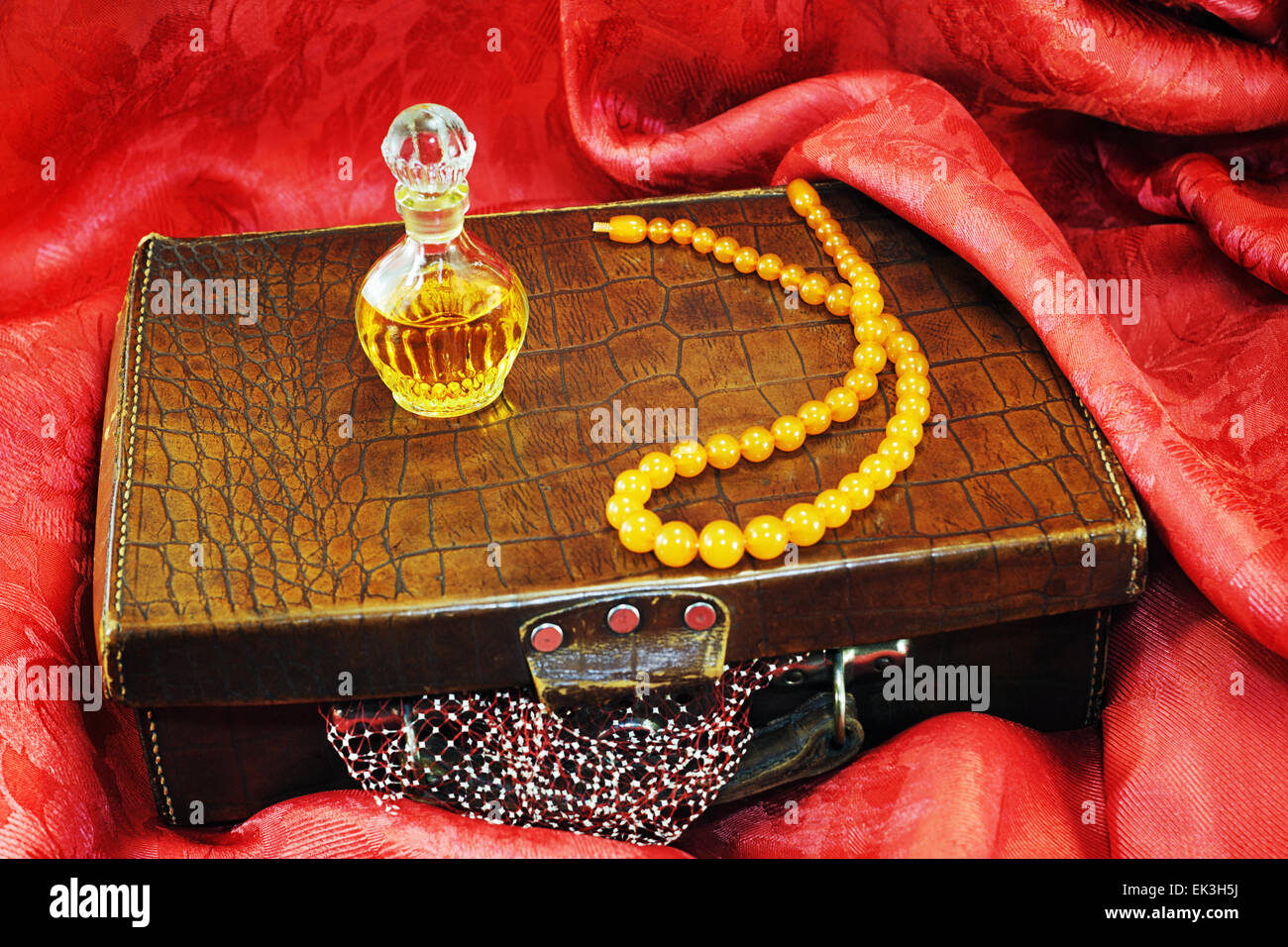 Valise vintage, collier d'ambre, flacon de parfum sur de vieux textiles rouge Banque D'Images