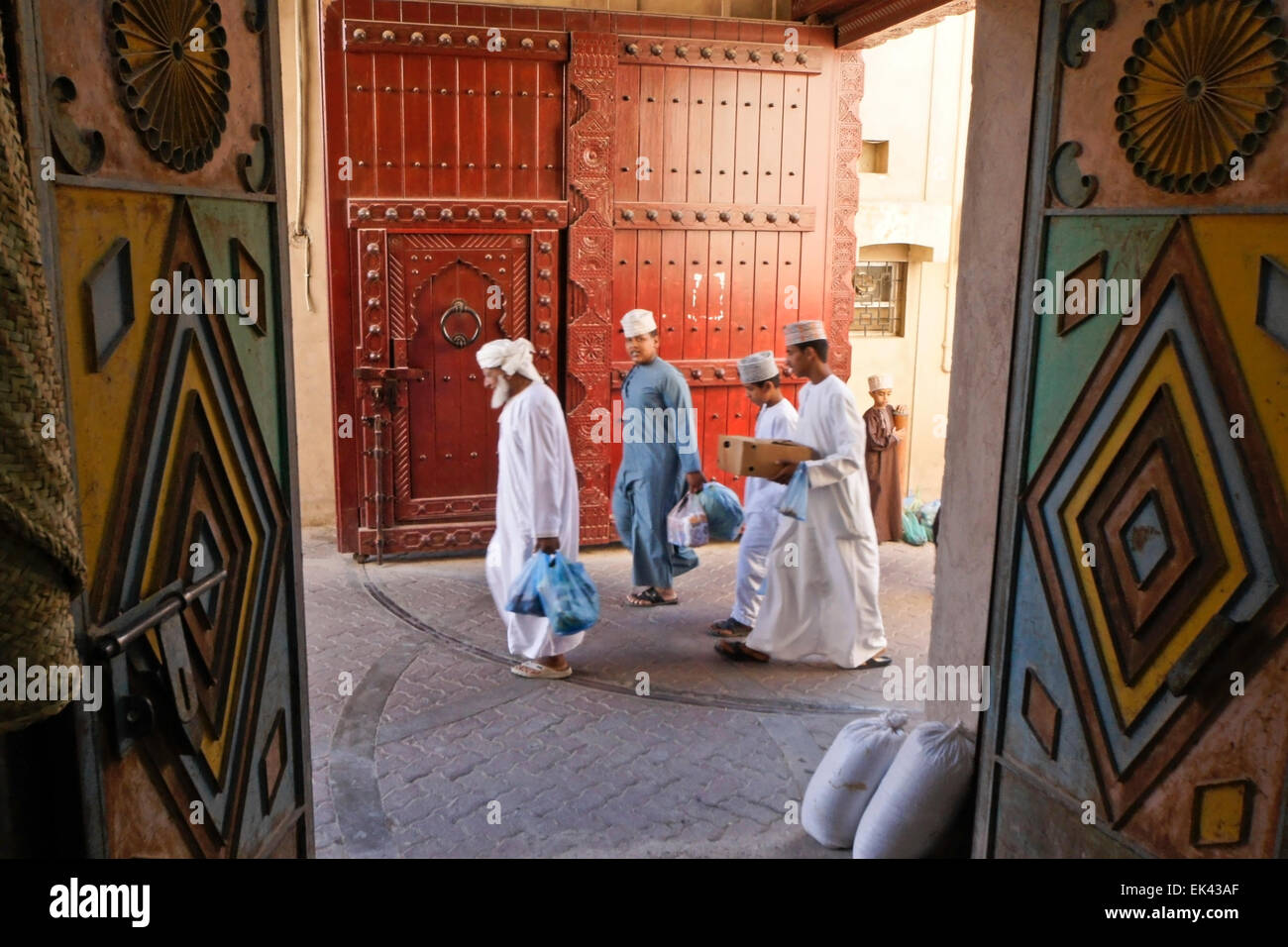 Les mâles omanais passé belle porte en marche, le souk de Nizwa, Oman Banque D'Images