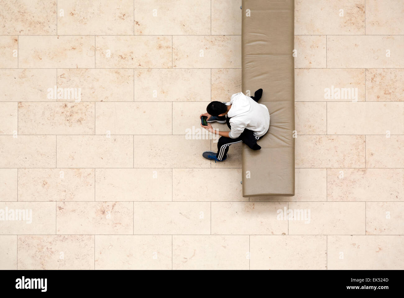 Garçon assis sur le banc du Musée avec téléphone. Jeu dans les mains. À partir de ci-dessus. Banque D'Images