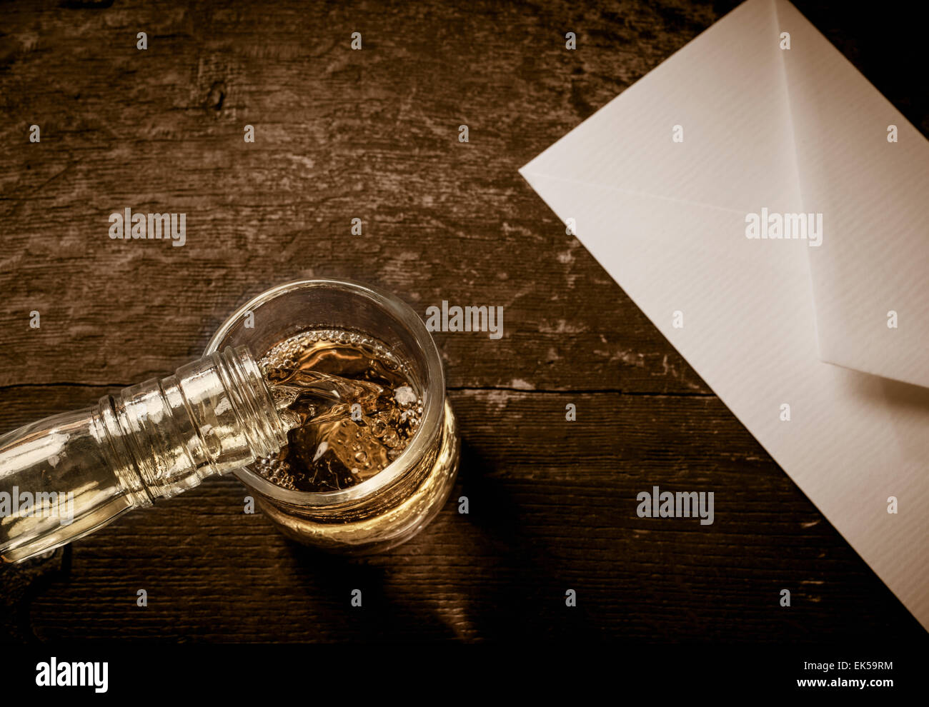 Bouteille de whisky verser dans un verre. Le verre est placé sur une table en bois rustique avec une enveloppe blanche à côté de Banque D'Images