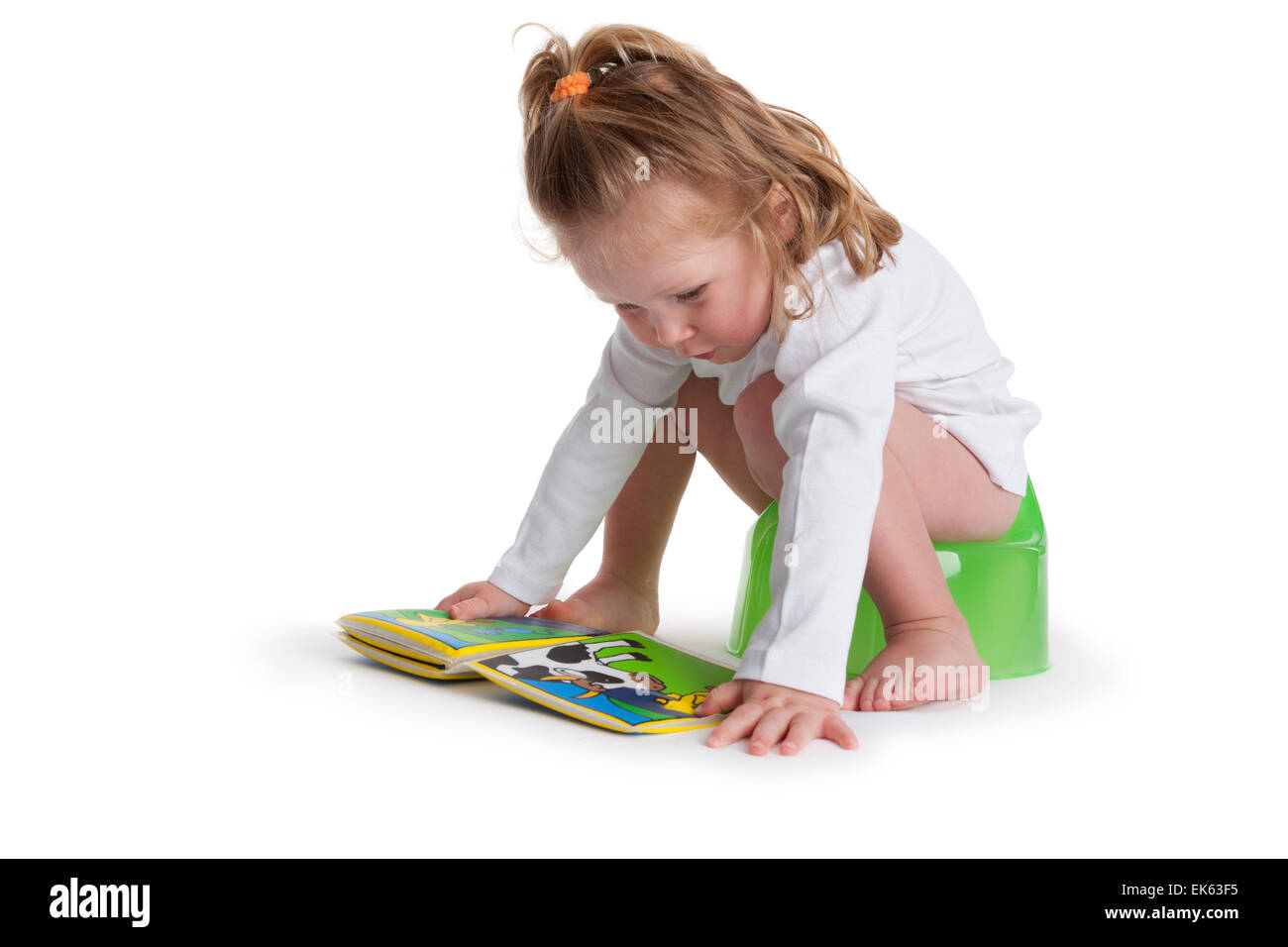 Trois ans, assis sur un pot et lit un livre d'images sur fond blanc Banque D'Images