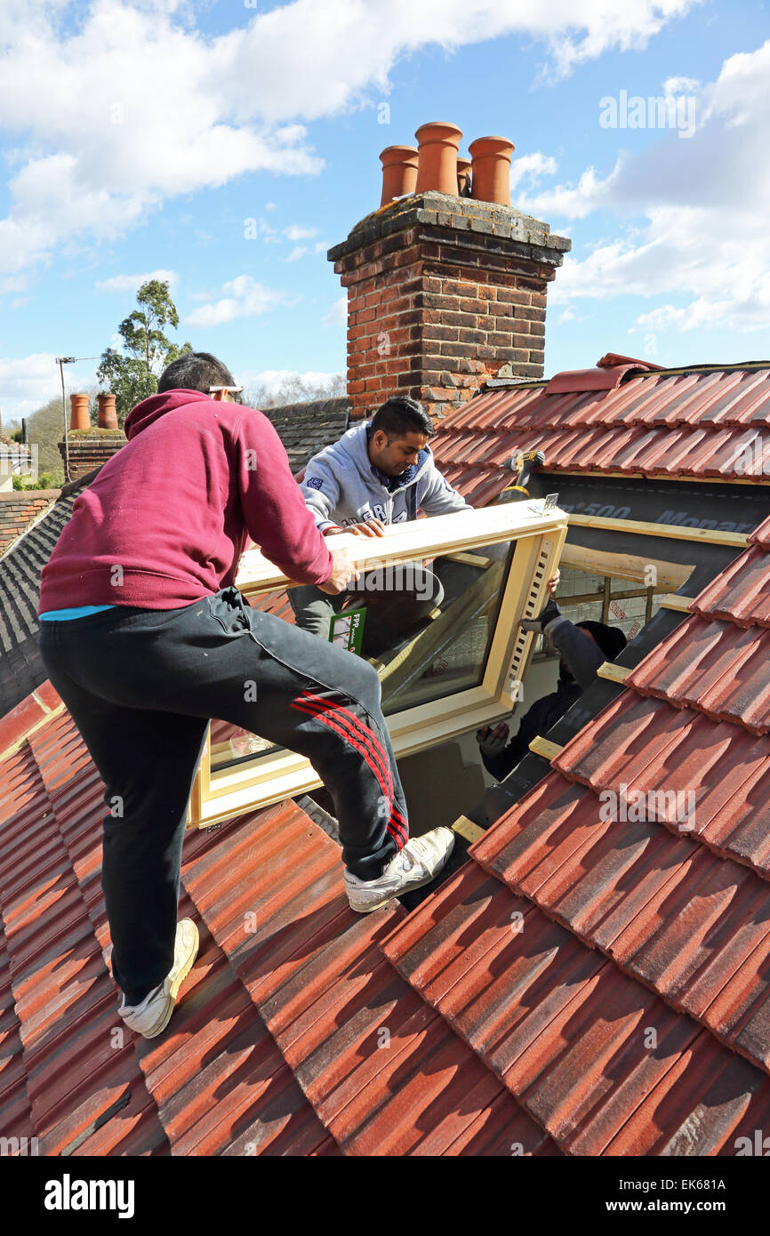 Les constructeurs étrangers l'installation d'une fenêtre de toit sur une toiture de tuiles dans le sud de Londres Banque D'Images