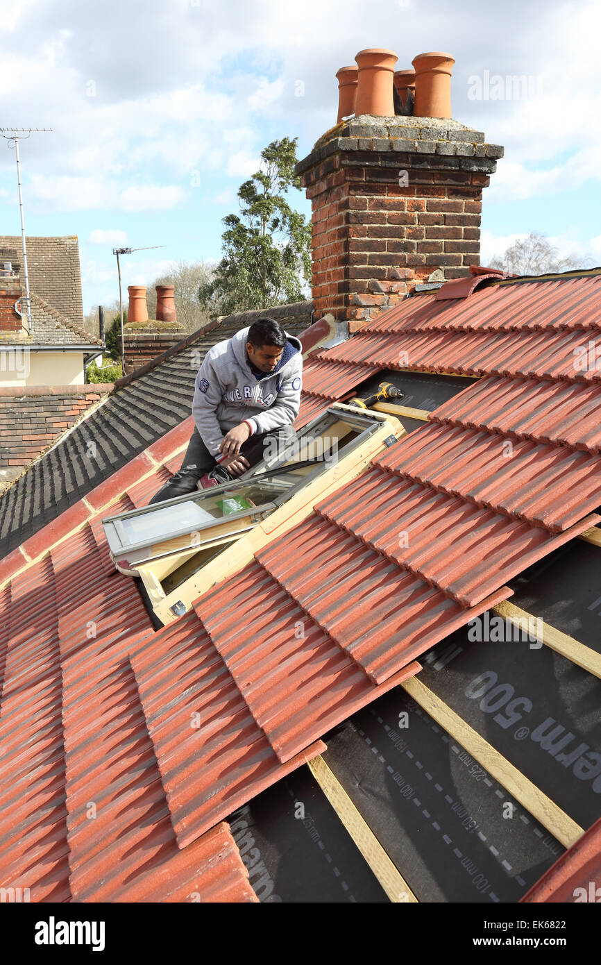 Un constructeur de l'installation d'un velux sur un toit aigu dans le sud de Londres Banque D'Images