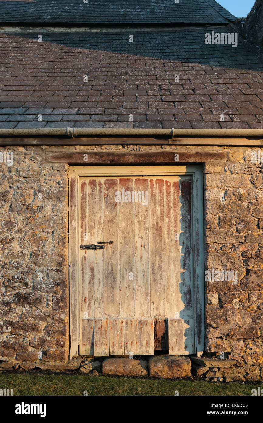 Vieille porte de grange en décomposition dans mur en pierre avec toiture en ardoise Banque D'Images