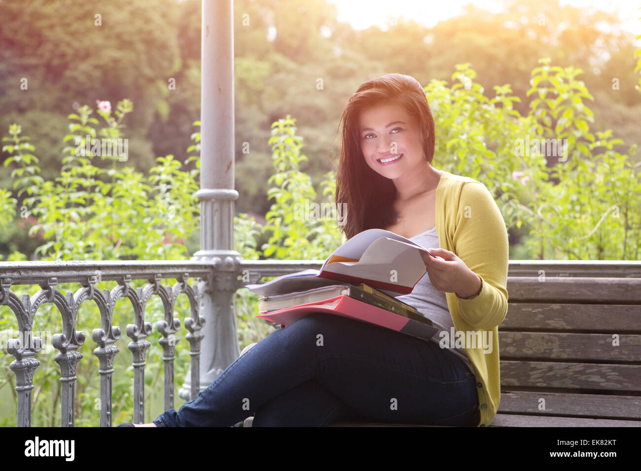 Belle jeune femme à l'université avec des livres et des dossiers sur les genoux, assis sur le banc en bois sous pergola dans un parc. Banque D'Images