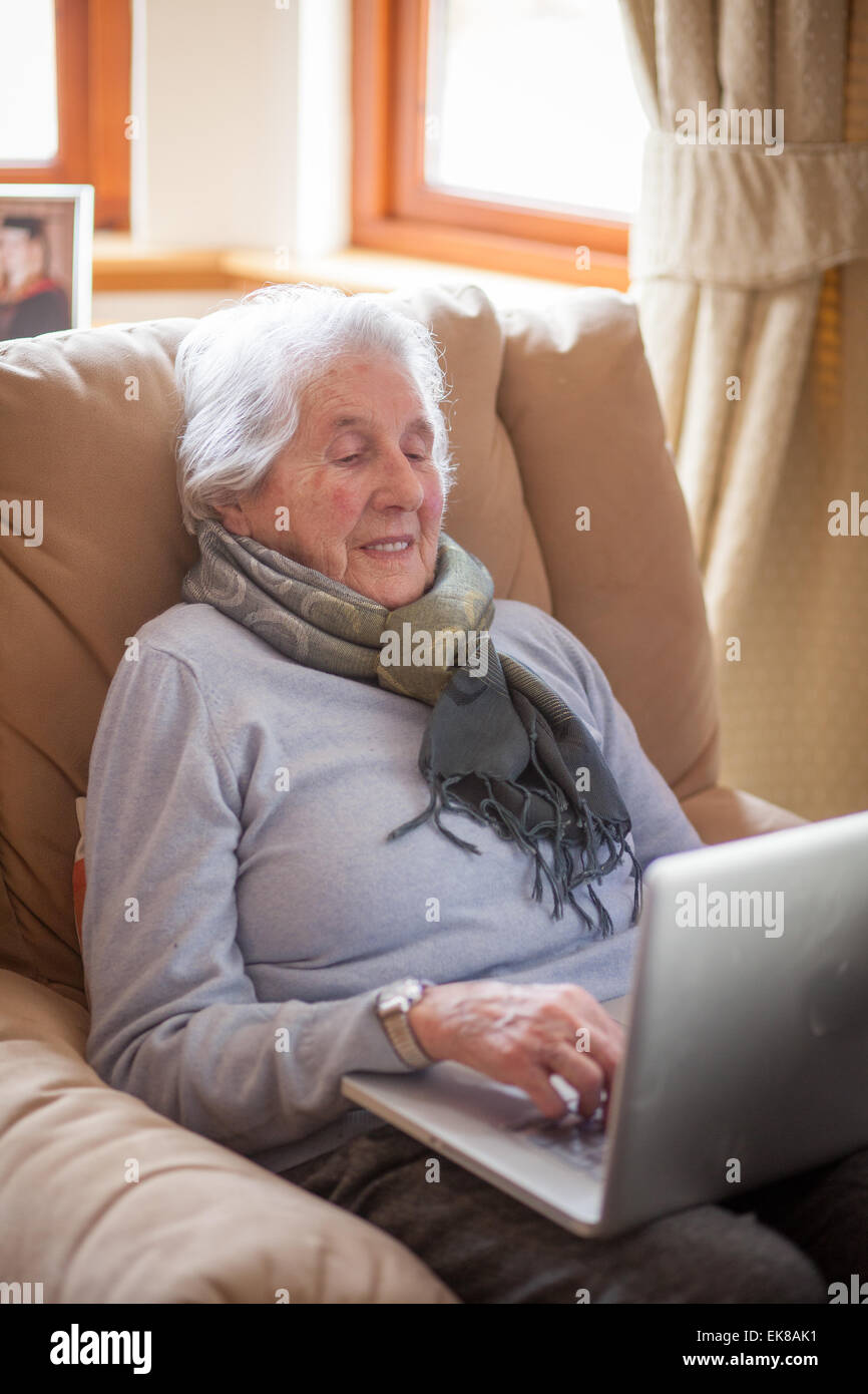 Vieille dame assise dans un fauteuil à l'aide d'un ordinateur portable. Banque D'Images