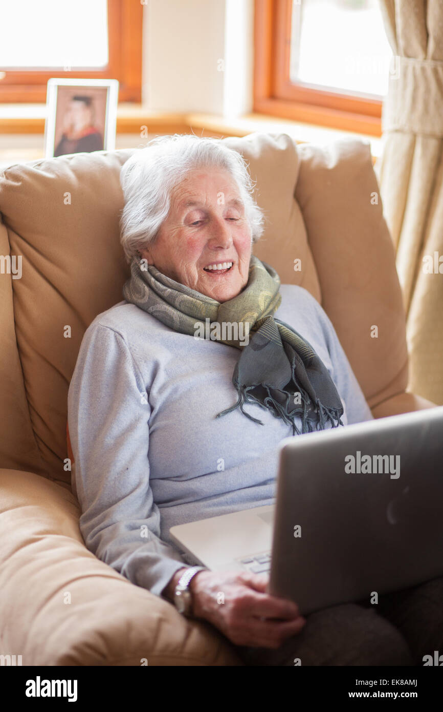 Vieille dame assise dans un fauteuil à l'aide d'un ordinateur portable. Banque D'Images