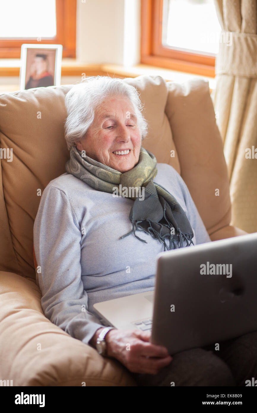 Vieille dame assise dans un fauteuil à l'aide d'un ordinateur portable. Banque D'Images