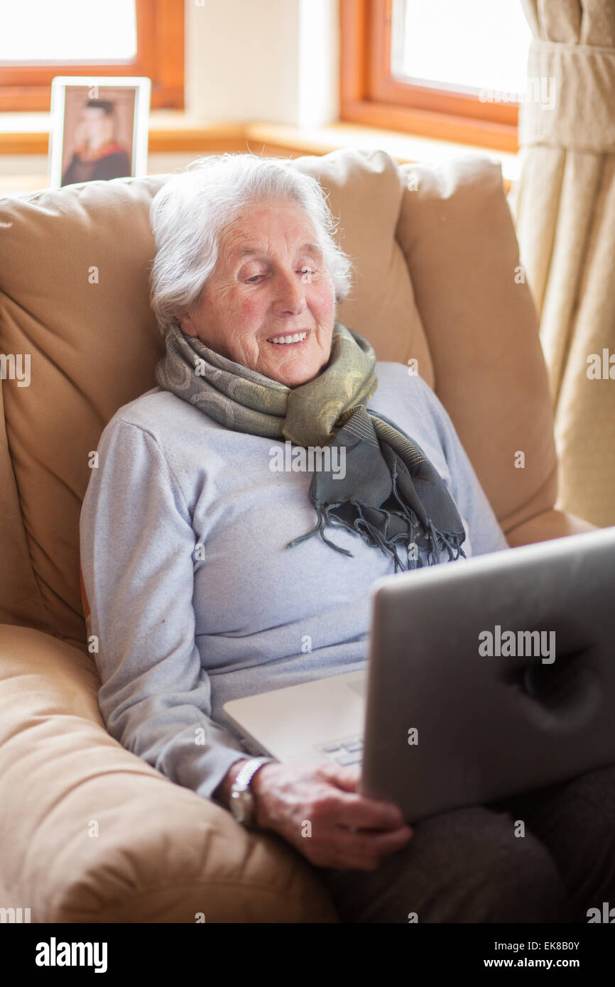 Vieille dame assise dans un fauteuil à l'aide d'un ordinateur portable. Banque D'Images