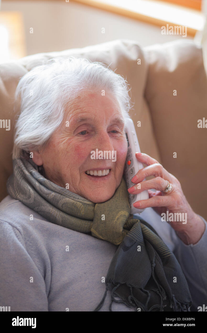 Vieille dame assise dans un fauteuil à parler au téléphone Banque D'Images