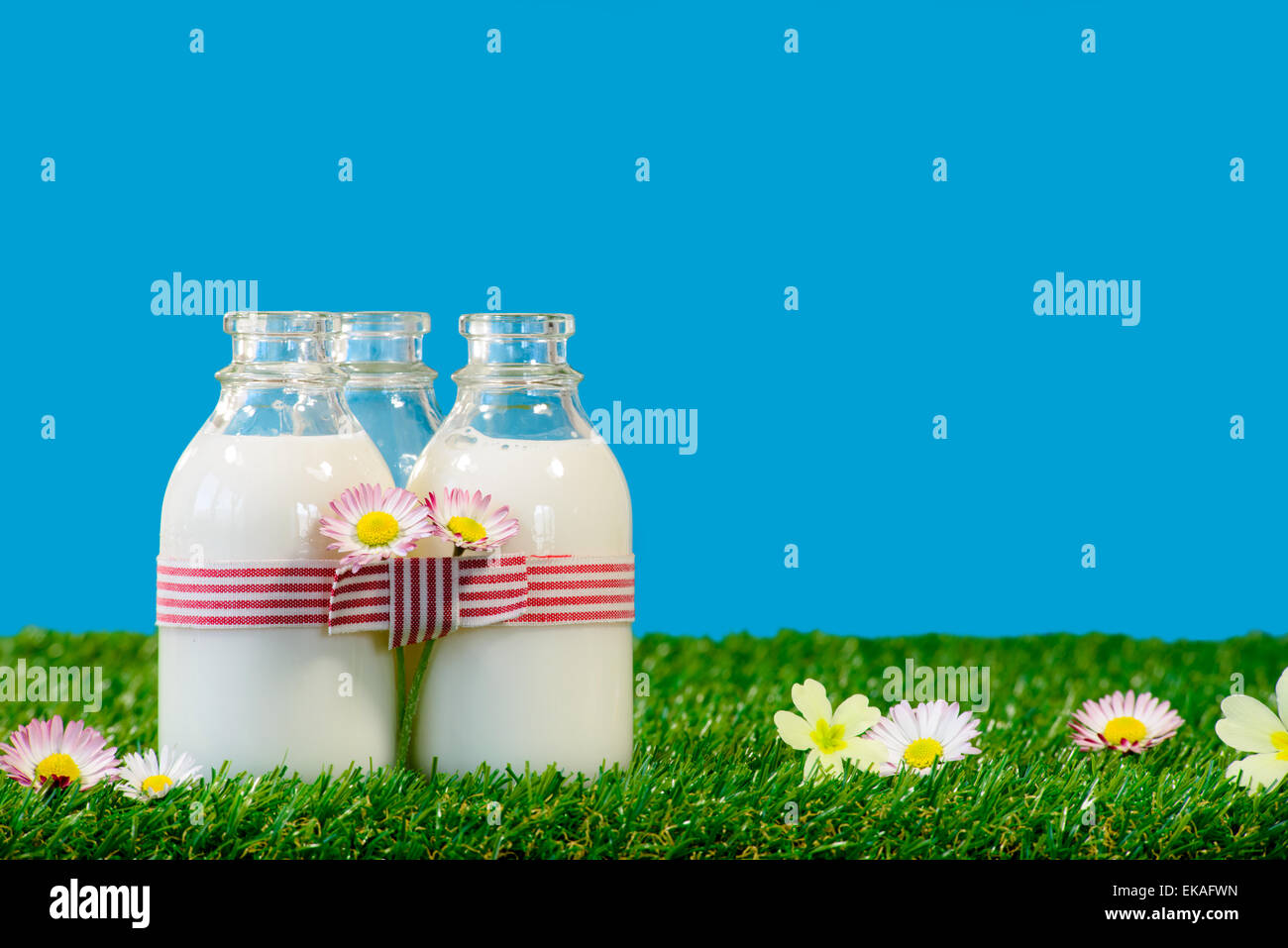 Trois petites bouteilles de lait dans un pré avec ciel bleu Banque D'Images