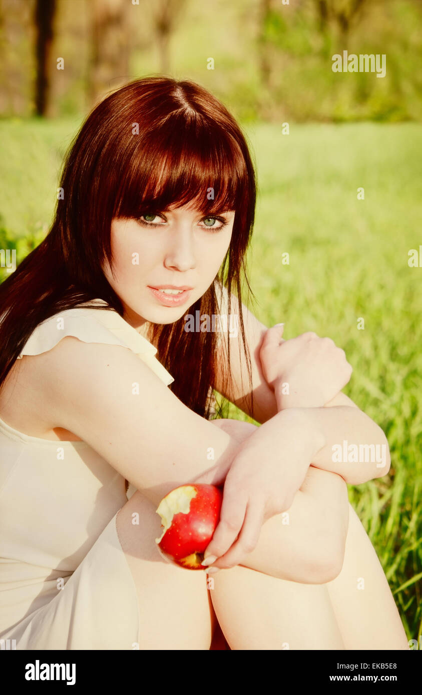 Belle jeune fille assise sur l'herbe avec Apple dans la main Banque D'Images