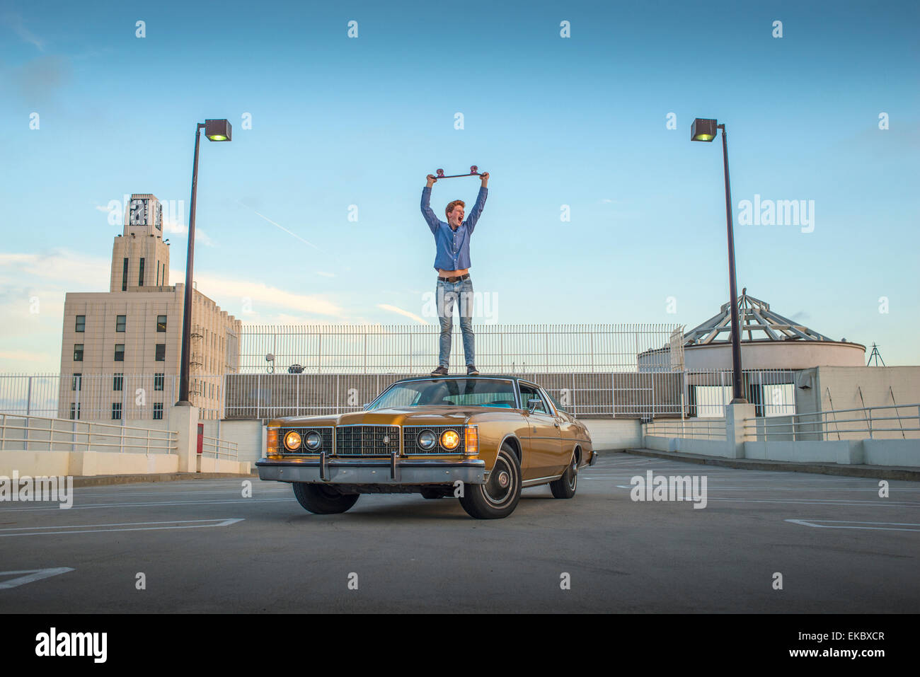 Portrait de jeune homme debout sur la voiture au-dessus de la tête de planche à roulettes Banque D'Images