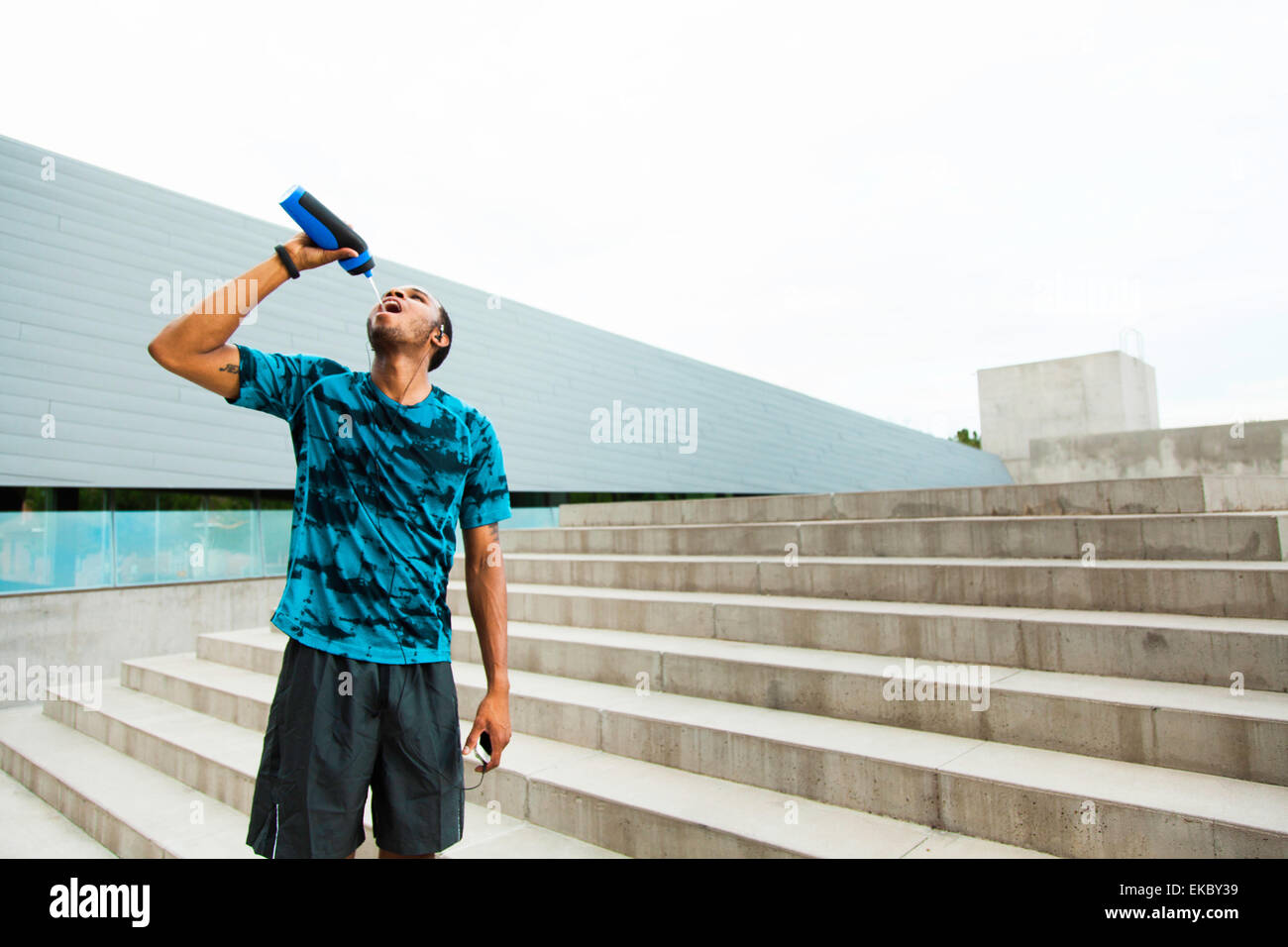Young male runner l'eau potable sur les étapes de la ville Banque D'Images