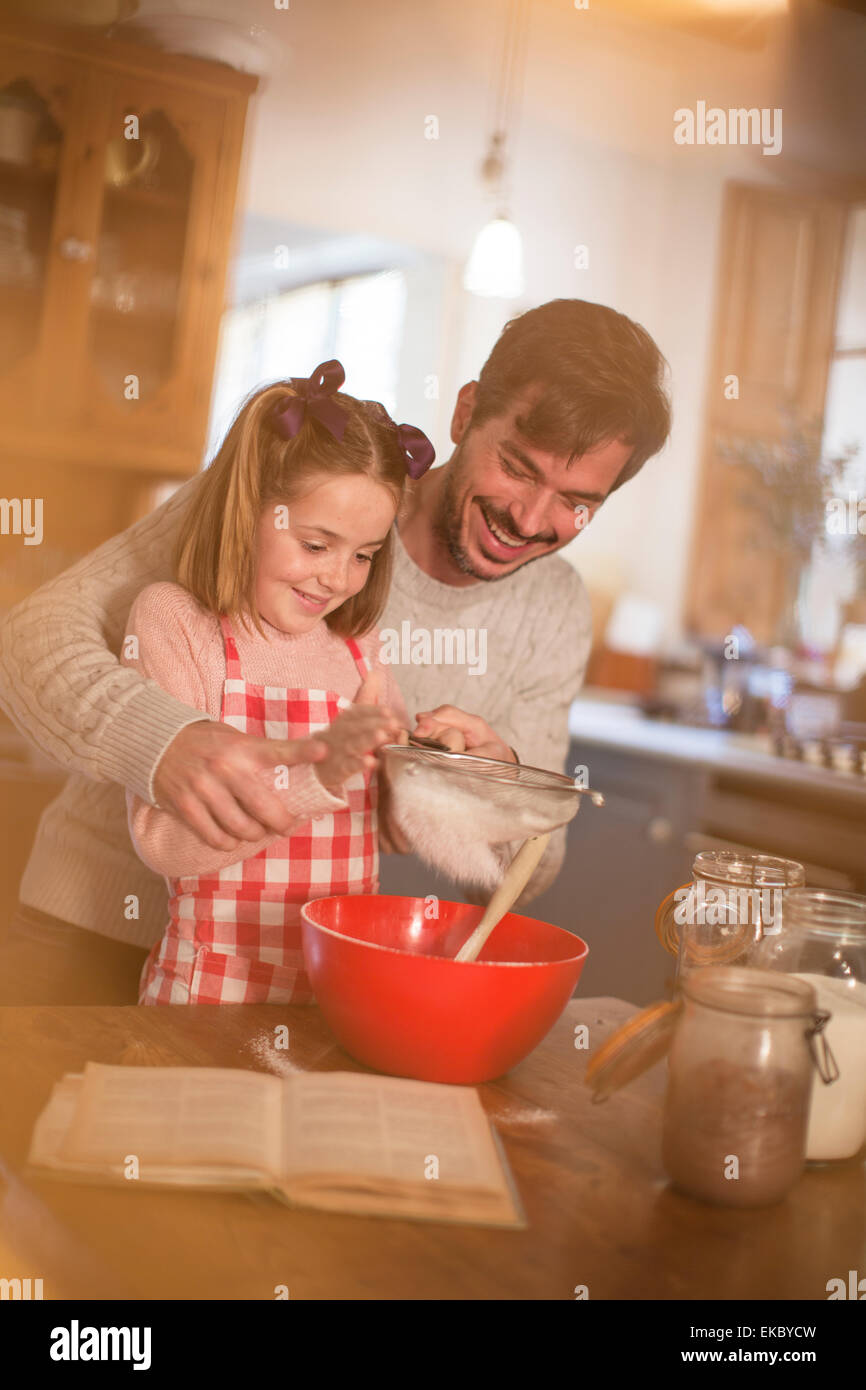 Père et fille tamisant la farine dans un récipient Banque D'Images