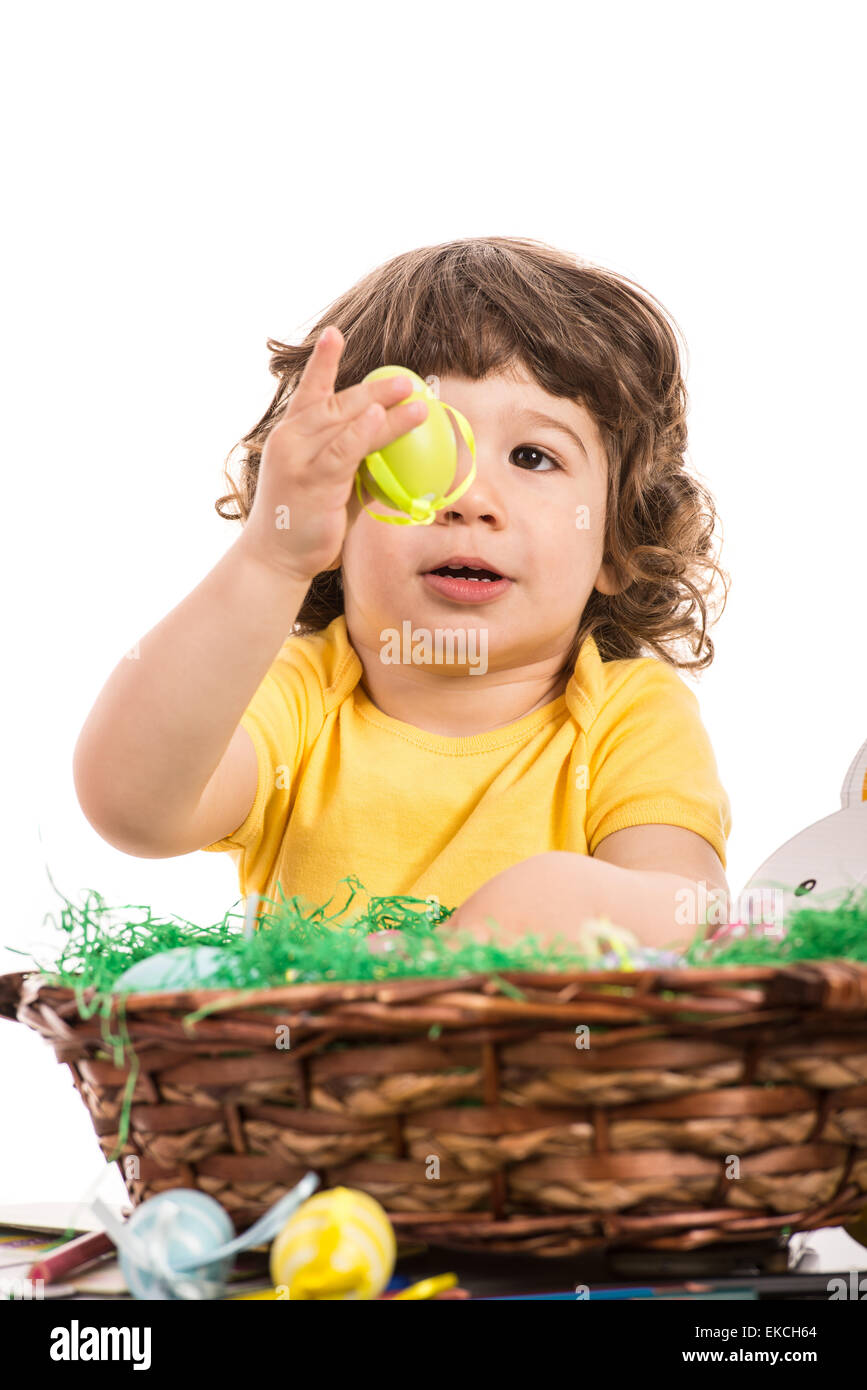 Bébé garçon montrant à la recherche et à l'oeuf jaune à partir d'un panier avec des œufs de Pâques isolé sur fond blanc Banque D'Images