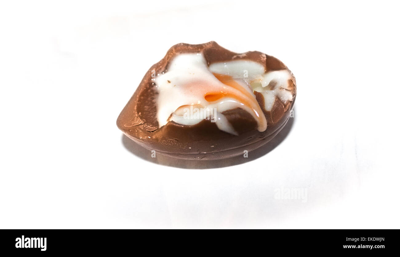 Un œuf en chocolat rempli à moitié mangé avec du sucre blanc d'oeuf et le jaune d'œuf se répandre au remplissage de la côte sur un fond blanc. Banque D'Images