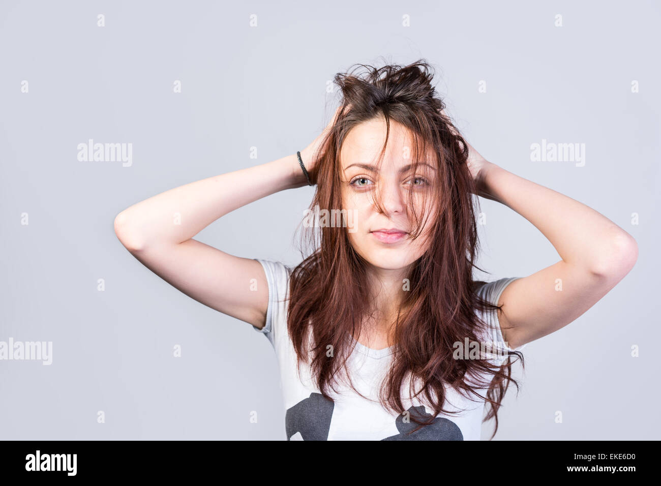 Close up Young Woman Holding ses longs cheveux en désordre en regardant sérieusement l'appareil photo sur un fond gris. Banque D'Images