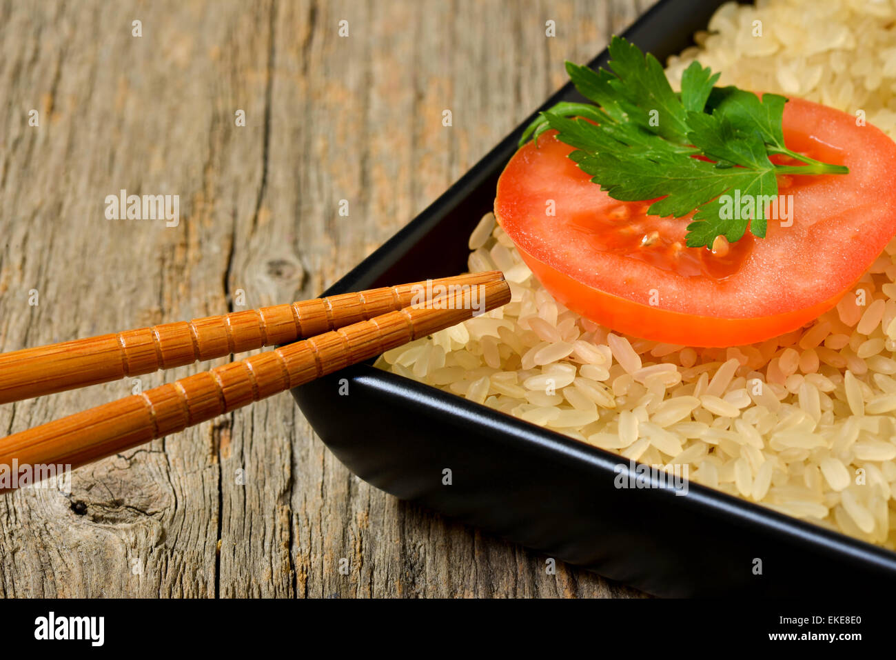 Plaque avec riz non cuit et tranche de tomate Banque D'Images