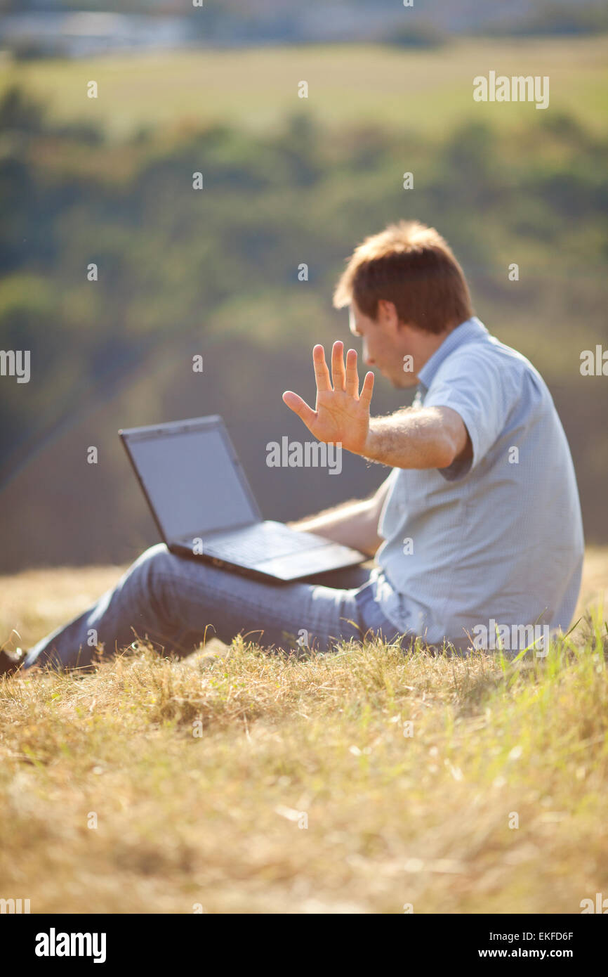 Young man using laptop assis sur l'herbe sur la colline Banque D'Images