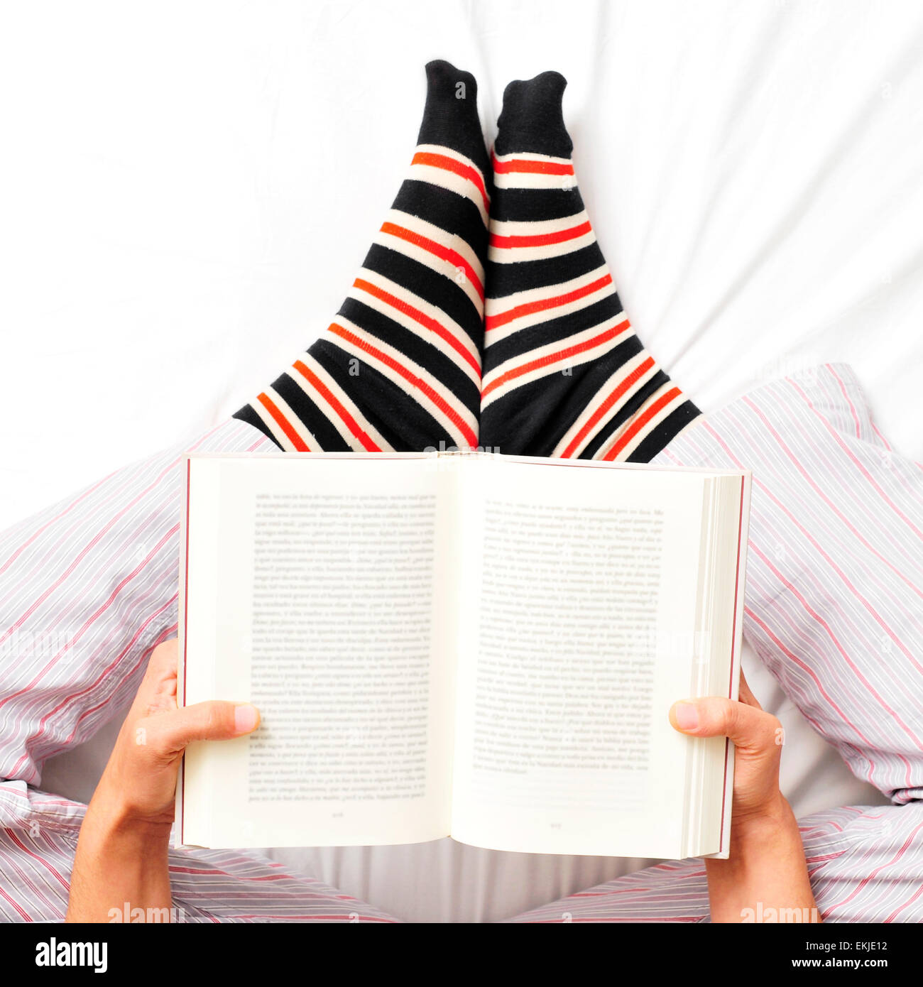 Un grand angle shot of a young man wearing pyjamas et chaussettes à rayures lit un livre au lit Banque D'Images